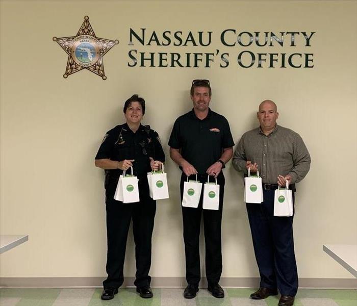 Cory Palmer and two members of Nassau County Sheriff's Department holding gift bags and standing in front of department sign.