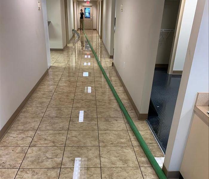 Photo showing water on floor of a long hallway with SERVPRO tech performing extraction